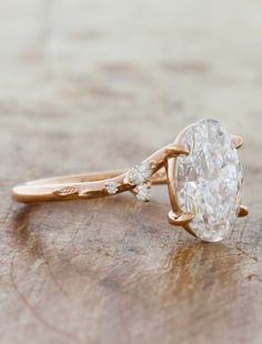 an oval shaped diamond ring on top of a piece of wood with two small diamonds