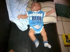 a baby laying on top of a black couch next to a blue and white blanket