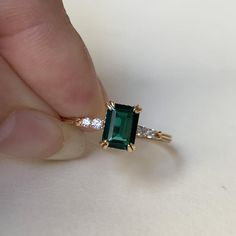 a person is holding an emerald and diamond ring