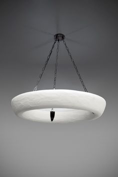 a white circular light fixture hanging from a metal chain over a gray wall and floor