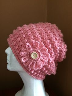 a pink crocheted hat with a flower on it sitting on a mannequin head