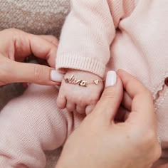 a woman holding a baby's name ring in her hands while she is wearing a pink sweater