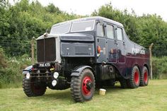 an old truck is parked in the grass near some bushes and trees with red rims