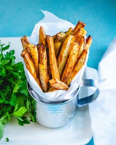 french fries in a tin with parsley next to it on a white plate and blue background