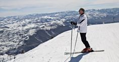 a man standing on top of a snow covered slope with skis and ski poles