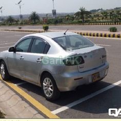 a silver car parked in a parking lot next to a yellow line and palm trees