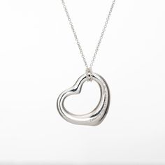 Stylish pre-owned Tiffany & Co Open Heart necklace crafted in sterling silver.    The simple and elegant design by Elsa Peretti celebrates the spirit of love. The Tiffany & Co sterling silver chain measures 16 inches and is great worn alone or layered with your fine jewelry from any era. Also included is a Tiffany & Co travel pouch.   The necklace is in very good original condition and was lightly cleaned and polished.  Particulars:  Weight: 5.6 grams  Stones:  N/A.  Size & Measurements: The necklace measures 16 inches in length. The pendant measures 22mm diameter (0.86 inches).  Metal & Hallmark: Sterling silver. The necklace is hallmarked "Ag 925" and "Tiffany & Co". The pendant is also hallmarked "Tiffany & Co" and "925" for sterling silver and "Spain". Tiffany And Co Silver Necklaces, Chanel Pendant, Purple Pendant Necklace, Art Deco Pendant Necklace, Blue Pendant Necklace, White Gold Pendant Necklace, Sapphire Necklace Pendants, Open Heart Necklace, Elsa Peretti