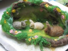 three small stuffed animals are in a miniature garden setting on a white cloth covered napkin