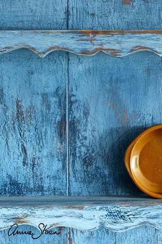 an orange bowl sitting on top of a wooden shelf next to blue painted wood planks