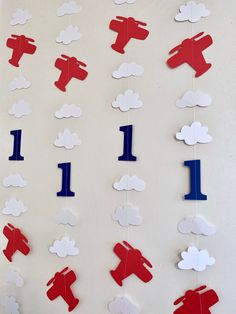 red, white and blue paper airplanes are hanging on a wall with clouds in the background