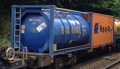 a blue and orange train with tanker cars on the tracks in front of some trees