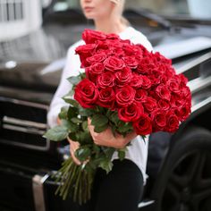 a woman is holding a large bouquet of red roses