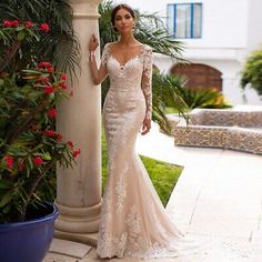 a woman in a wedding dress standing next to a pillar and flower potted plant