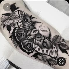 a black and white photo of a moth tattoo on the arm, with leaves around it