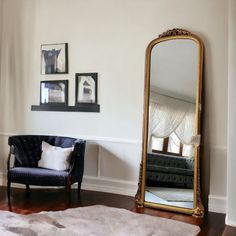 a living room with a chair, mirror and pictures on the wall in it's corner