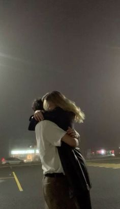 two people hugging each other in the middle of an empty parking lot at night time