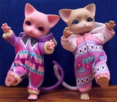 two figurines of cats dressed in pajamas on a wooden table next to a blue wall