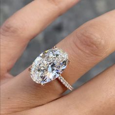 a woman's hand with a diamond ring on top of her finger and an oval shaped diamond in the middle