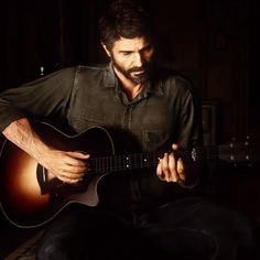 a man with a beard is playing an acoustic guitar in the dark while sitting down