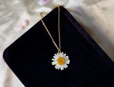 a white and yellow daisy necklace on a black velvet case with gold chain hanging from it