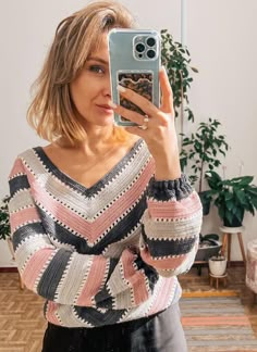 a woman taking a selfie with her cell phone in front of her, wearing a colorful sweater and black leather skirt