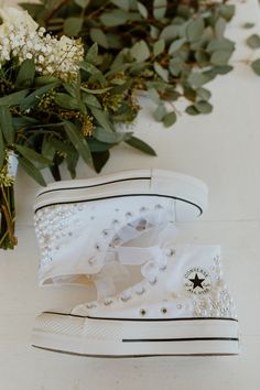 two white converse sneakers with flowers and greenery in the background, on a table