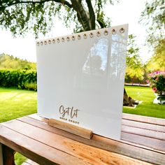 an open notebook sitting on top of a wooden bench in front of a green field