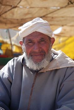 an old man with a white turban on his head sitting under a tent