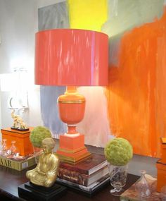 an orange lamp sitting on top of a wooden table next to a painting and vases