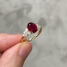 a person is holding a ring with a red stone and white diamonds on it's side