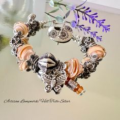 This exquisite Bohemian style glass bead Butterfly Charm bracelet is crafted with 12mm Artisan Lampwork glass bicone beads in a stunning peachy/orange base encased in clear glass by glass artist Lynda Cogbill, each adorned with Karen Hill Tribes Silver bead caps. Featuring a 12mm ornate Karen Hill Tribe Silver focal bead at the center, oxidized to reveal intricate pattern detail, accompanied by a Karen Hill Tribe Silver Butterfly Charm and tiny orange Sapphire Charm symbolizing change, growth, h Apricot Beaded Round Bead Jewelry, Handmade Adjustable Peach Bracelets, Handmade Apricot Jewelry With Round Beads, Elegant Handmade Coral Beaded Bracelets, Handmade Bohemian Apricot Jewelry, Handmade Apricot Round Bead Jewelry, Handmade Apricot Bohemian Jewelry, Bohemian Nickel-free Charm Bracelet With Round Beads, Handmade Peach Beaded Bracelets As Gift