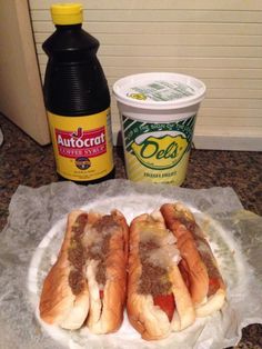 two hot dogs sitting on top of a paper plate next to a container of mustard and ketchup