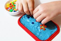 a child's hands playing with beads in a blue tray on a white table