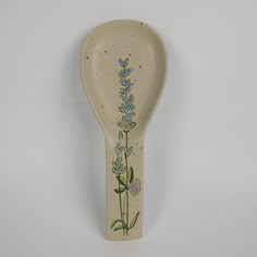 a ceramic spoon with a flower painted on it's side, hanging from the wall