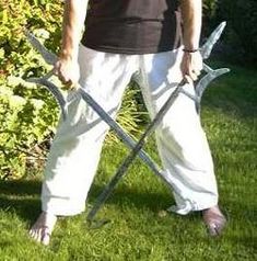 a man standing in the grass holding two large irons and wearing white pants with his hands behind his back