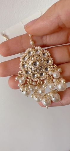 a hand holding a gold and white necklace with pearls hanging from it's center