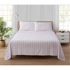 a bed with pink and white striped bedspread next to a potted plant