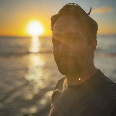 a man standing on top of a beach next to the ocean at sun rise in the background