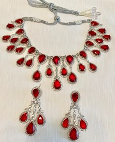 Enhance your jewelry collection with our CZ American Diamond and Red Stone Necklace set. This elegant set is perfect for any party or special occasion. The combination of CZ diamonds and red stones adds a touch of sophistication and glamour. Up your style game and stand out from the crowd with this stunning necklace set. Jewellery Care- Keep the jewellery dry, avoid contact with perfumes and water. Red Party Jewelry With Jewels, Red Crystal Necklaces For Celebrations, Elegant Red Rhinestone Necklaces, Red Jeweled Jewelry Set For Celebration, Red Crystal Bridal Necklace For Party, Red Crystal Party Necklace, Formal Cubic Zirconia Jeweled Jewelry Sets, Formal Jeweled Cubic Zirconia Jewelry Sets, Red Crystal Jewelry With Rhinestones