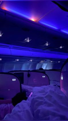 the interior of an airplane with purple lights and white sheets on it's bed