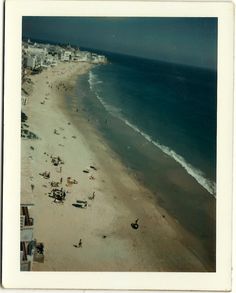 an aerial view of people on the beach and in the water, with buildings behind them