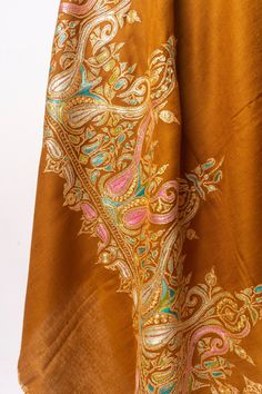 Wrap yourself in the warm embrace of autumn with this "Sozni Tilla Splendor Pashmina," a testament to timeless grace and artistry. Each thread of this luxurious pashmina has been tenderly hand-embroidered with the intricate sozni needlework, which dances along the fabric in harmonious golds and spirited pastels, reminiscent of Kashmir’s enchanting fall season. This pashmina is not merely an accessory; it is a piece of heritage, handcrafted with tilla, the golden touch that turns every drape into Pashmina Shawl Embroidery Hands, Brown Embroidered Pashmina Shawl, Festive Brown Dupatta With Intricate Embroidery, Bohemian Pashmina Scarves With Floral Embroidery, Traditional Brown Silk Shawl, Silk Shawl With Intricate Embroidery, Traditional Embroidered Silk Scarf, Brown Dupatta With Intricate Embroidery, Embroidered Pashmina Shawl In Traditional Drape