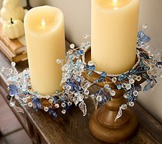 two candles are sitting on a table next to a candle holder with flowers and leaves