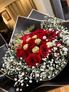 a bouquet of red roses and white flowers with chocolates in the middle on a table