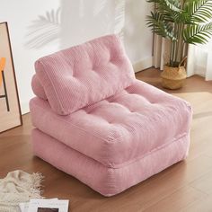 a pink chair sitting on top of a wooden floor next to a potted plant