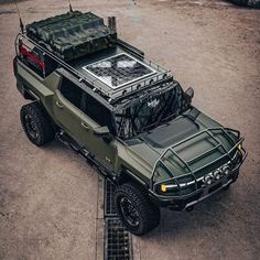 an army truck parked in the middle of a parking lot with its hood up and luggage on top