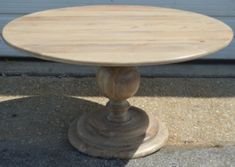 a round wooden table sitting on top of a cement floor next to a garage door