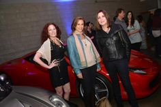 two women standing next to a red sports car