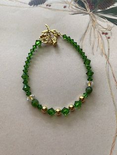 Green Swarovski delicate crystal bracelet with diamond shaped sparkling crystals, gold plated beads, clear crystal beads & a gold plated flower clasp. Size 7 1/2". This bracelet would be a great Anniversary or Birthday gift and lovely to wear on a night out.  Keep bracelet away from chemicals, lotion or water. Gold Crystal Chain Bracelet As Gift, Elegant Crystal Bracelets With Spacer Beads, Elegant Crystal Bracelets With Faceted Beads, Faceted Gold Crystal Bracelet As Gift, Handmade Gold Crystal Beaded Bracelets, Elegant Crystal Beaded Bracelets With Faceted Details, Elegant Gold Beaded Bracelets With Czech Glass, Elegant Faceted Crystal Beaded Bracelets, Gold Crystal Bracelet For May Birthstone Gift