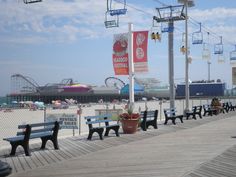 the boardwalk is lined with benches for people to sit and walk on, while roller coasters are in the background